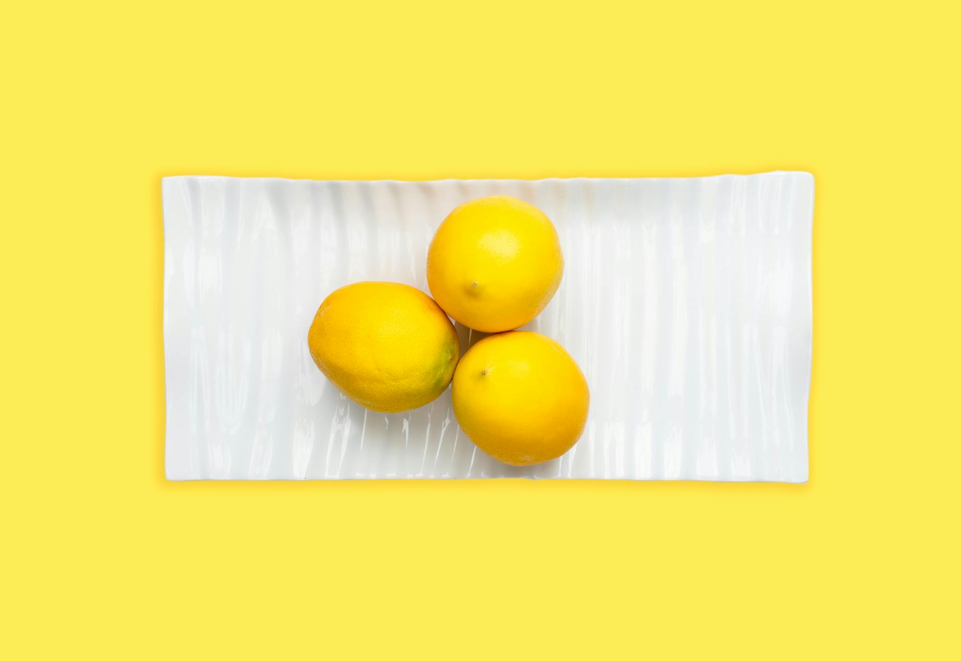 Fresh lemons arranged on a white plate with a vibrant yellow background, symbolizing the approachable nature of lemon vibrators