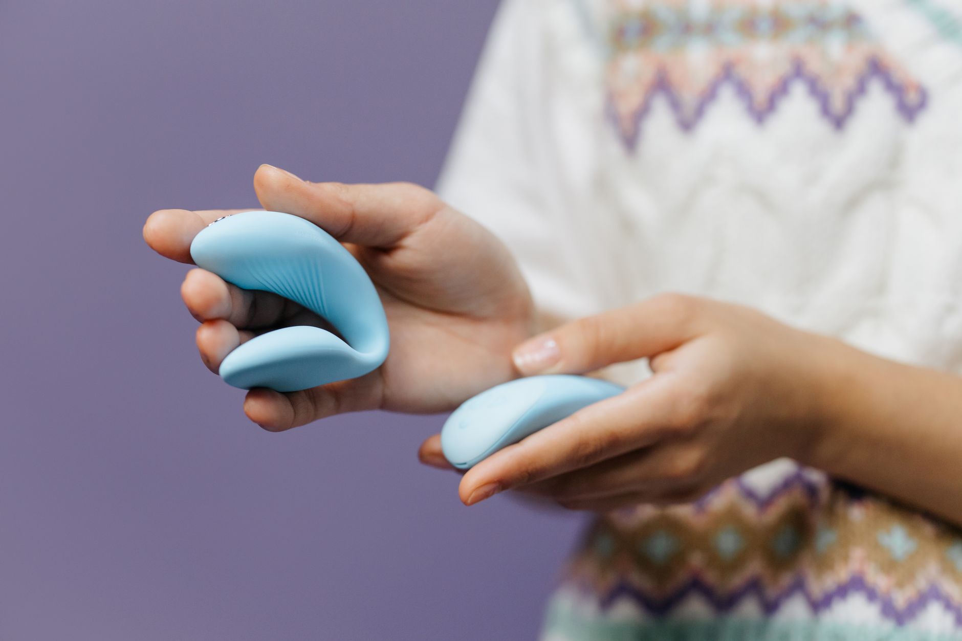 Primer plano de manos sosteniendo un vibrador azul brillante sobre fondo púrpura