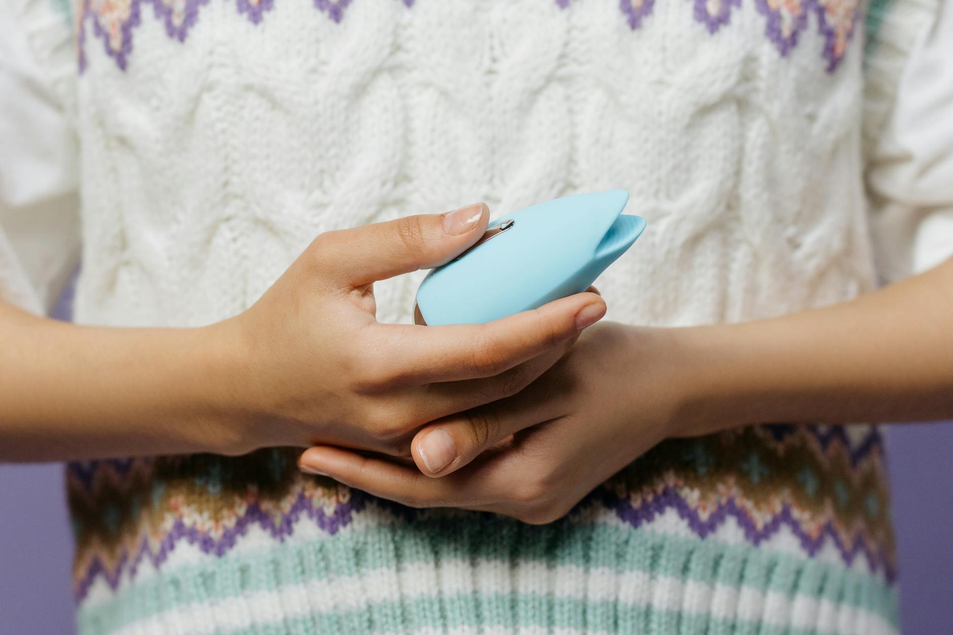 Primer plano de manos sosteniendo un vibrador azul contra un suéter tejido