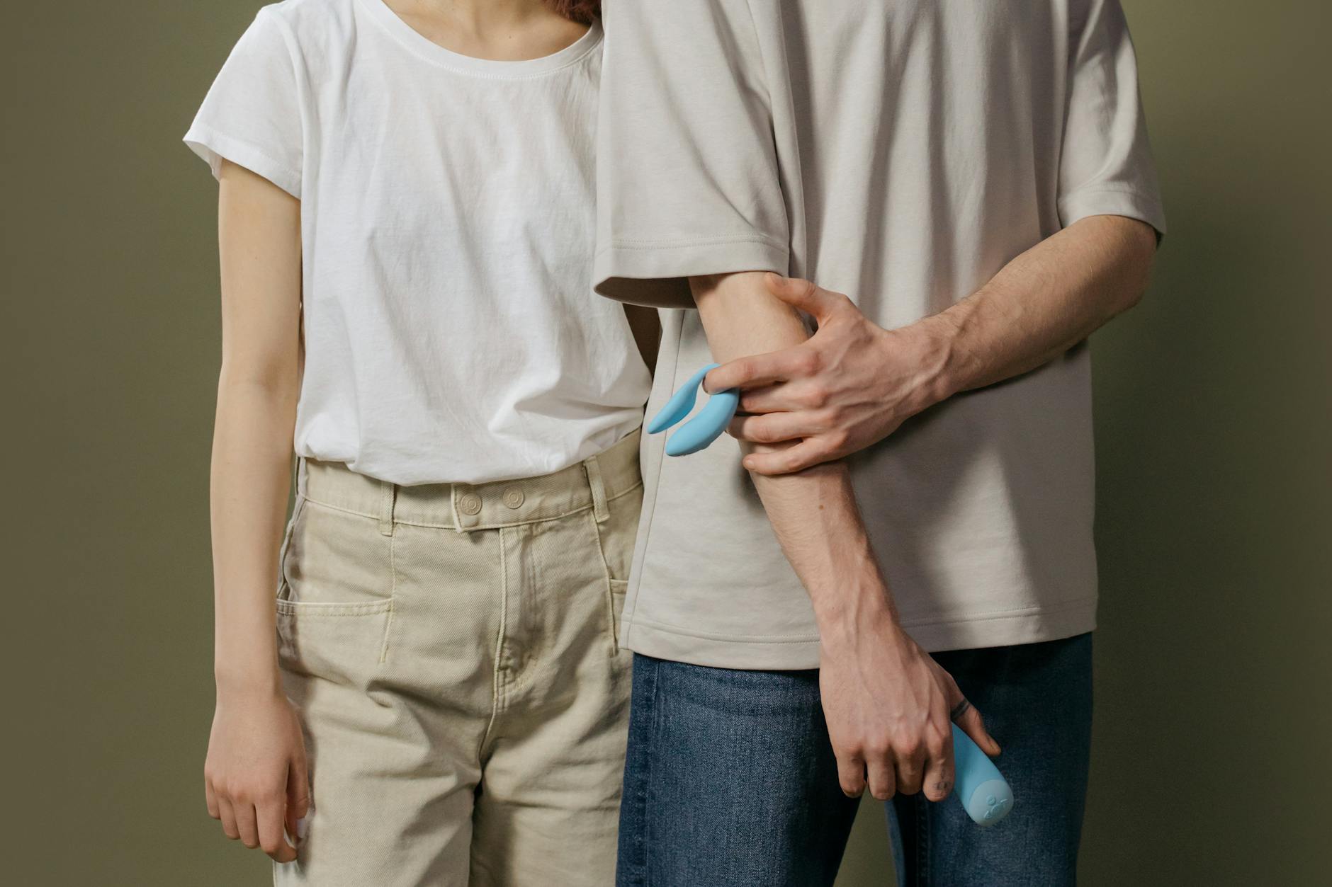 Pareja joven de pie juntos en un espacio minimalista, sosteniendo un vibrador azul, simbolizando la intimidad moderna